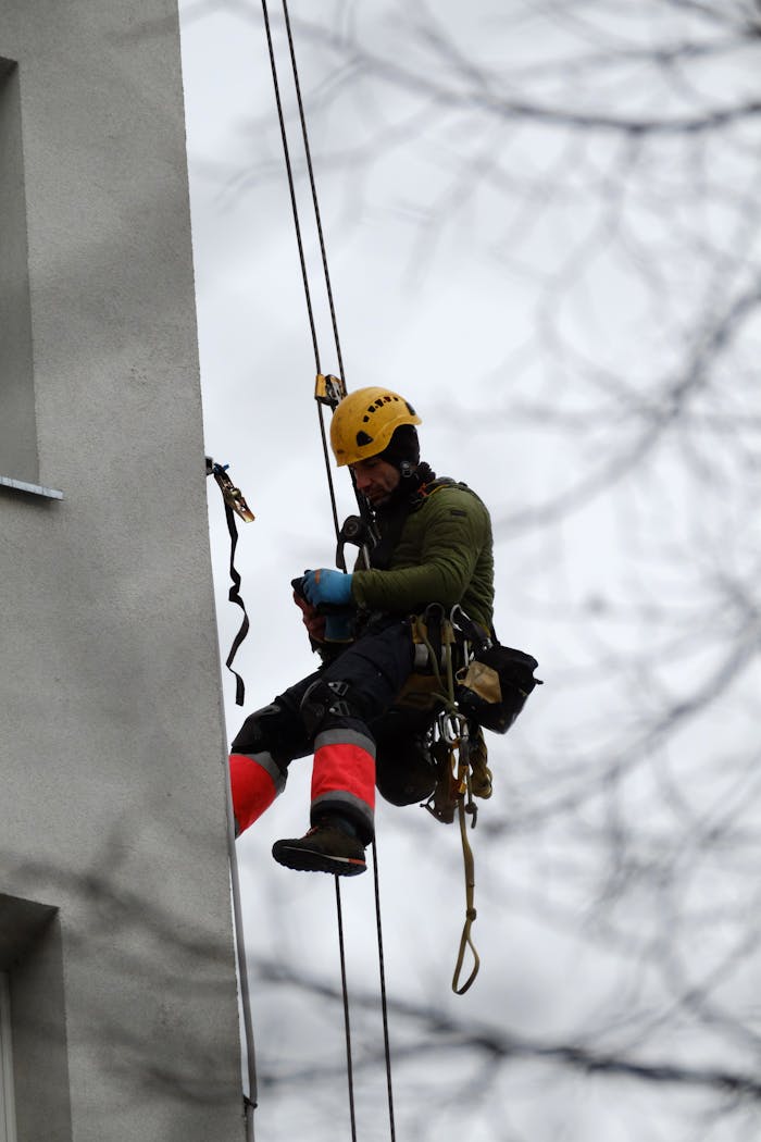 Rope access engineer in safety gear performing maintenance on building exterior during winter.