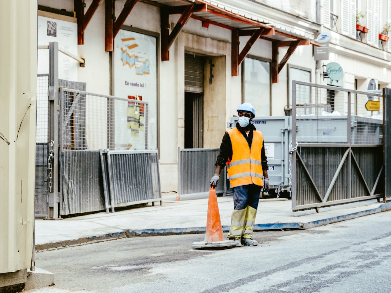 Construction worker wearing safety gear and holding a pylon on an urban street.